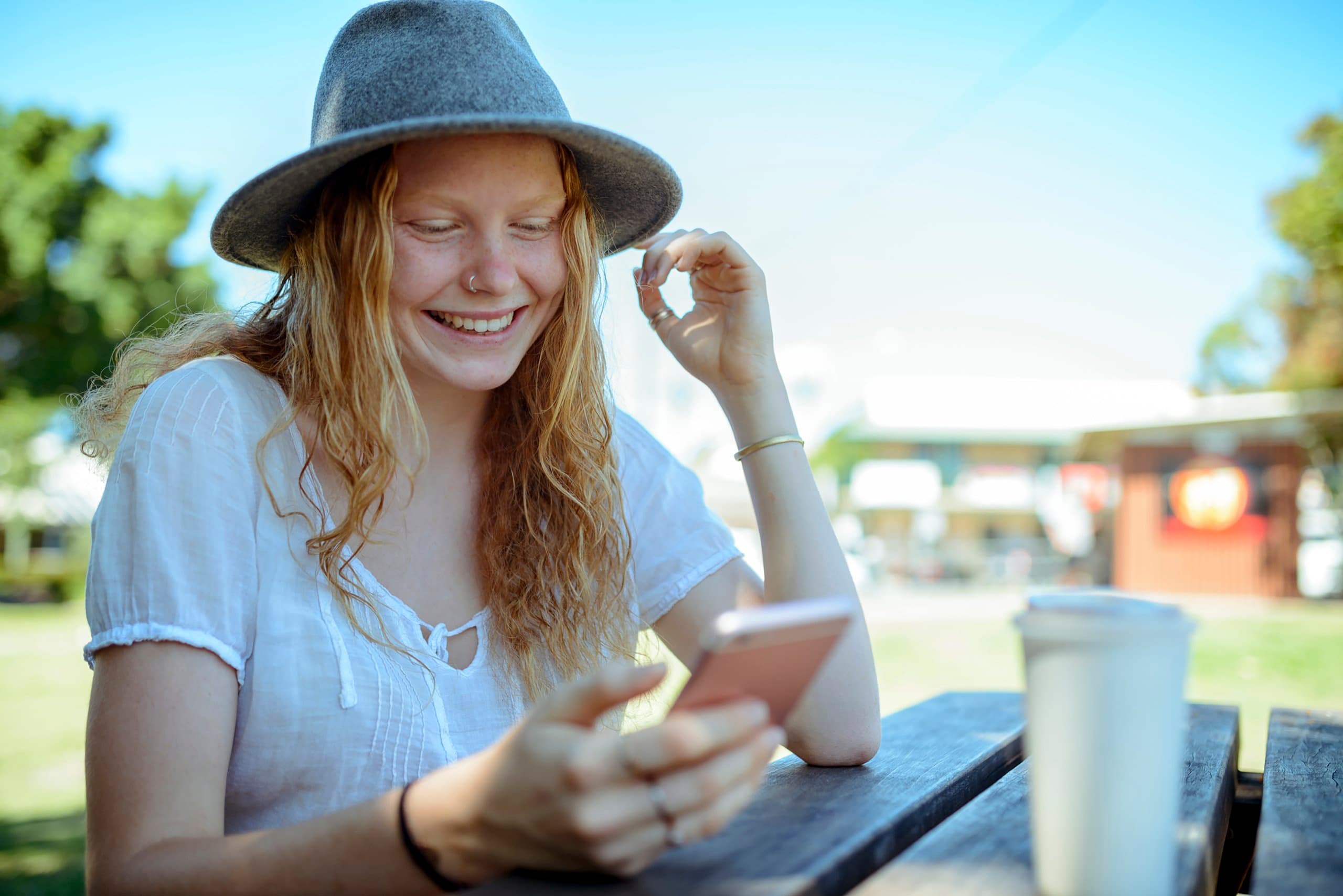 woman sitting smiling outside looking at phone